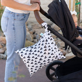 A parent pushes a stroller with a Bumkins Wet/Dry Bag: Hearts, made of waterproof fabric, hanging from the handle.