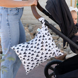 A person pushes a stroller with a Bumkins Wet/Dry Bag Set: Hearts, featuring black hearts, attached to the handle.