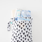 The Bumkins Wet Bag + Wet/Dry Bag Set: Hearts holds diapers, cream, and a book on a white surface.
