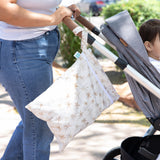A child sits in a stroller while a Bumkins Palm Daze Wet Bag hangs from the handle.