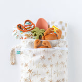 Bumkins Wet/Dry Bag: Palm Daze holds clothes, silicone toys, crab plush, and patterned cloth on a white background.