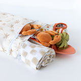 Bumkins Wet/Dry Bag: Palm Daze holds crab plush, baby clothes, a blanket, and sand toys on a white background.