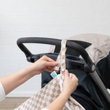 Hands attach a Bumkins Wet/Dry Bag: Sand Check, made of waterproof fabric, to a stroller using snap buttons on the strap.