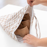 A child's hands open a Bumkins Wet/Dry Bag: Sand Check on a white table, revealing brown shoes inside.