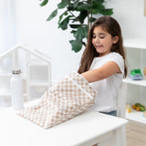 A smiling girl reaches into a Bumkins Wet/Dry Bag: Sand Check at a white table next to a water bottle with plant in the background.