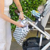 A woman places a gray toy cat into a Bumkins Wet/Dry Bag: Charcoal Check on a stroller with a child inside outdoors near greenery.