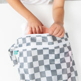 A child’s hands pack a diaper into the Bumkins Wet Bag + Wet/Dry Bag Set in Charcoal Check—ideal for on-the-go essentials.