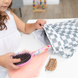 A child places a hairbrush and clip into a Bumkins Wet/Dry Bag: Charcoal Check on a white table.