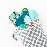 Bumkins Wet/Dry Bag: Charcoal Check with swim trunks, a towel, goggles, shoes, and teal swimsuit on a white background.