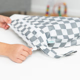 Hands zip a Bumkins Wet/Dry Bag: Charcoal Check on a white table.