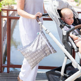 A woman pushes a stroller with a toddler; a Bumkins Lunar Phase Wet/Dry Bag hangs from the handle near water.