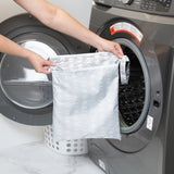A person holds a Bumkins Wet/Dry Bag: Lunar Phase in front of an open front-loading washing machine.