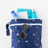 Bumkins Wet/Dry Bag: Evil Eye holds sunglasses, books, sunscreen, and a bottle on a white background.