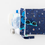 Bumkins Wet/Dry Bag: Evil Eye holds diapers, bottles, wipes & teal sunglasses on a white background.