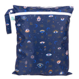 Bumkins Wet/Dry Bag: Evil Eye features celestial prints with eyes, stars, moons, and zodiac signs on dark blue waterproof fabric.