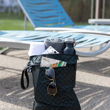 Roamio by Bumkins Wet/Dry Bag: Rich Black holds sunglasses, a book, towel, and water bottle by empty blue lounge chairs.