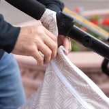 Close-up of a person attaching a Bumkins Wet/Dry Bag: Wander to a stroller handle outside.