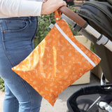 A person in jeans pushes a stroller outdoors with a Bumkins Wet/Dry Bag: Grounded attached to the handle.