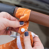 Close-up of hands with dark nail polish attaching a Bumkins Wet/Dry Bag: Grounded to a stroller handle using a snap button on the strap.