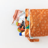 Bumkins Wet/Dry Bag: Grounded, filled with swimwear, flip-flops, sunscreen, and goggles, lays on a white background.