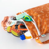 Close-up of Bumkins Wet/Dry Bag: Grounded with flip-flops, shorts, sunscreen, and goggles on a white background.
