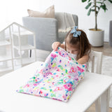 A young girl opens a Bumkins Wet/Dry Bag: Watercolor at a white table in a bright, modern living room.