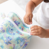 A child opens a vibrant Bumkins Wet/Dry Bag: Aloha Stitch at a white table.
