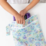 A child places a purple tablet into Bumkins Wet/Dry Bag: Aloha Stitch on a white table.