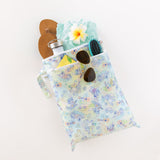 Bumkins Wet/Dry Bag: Aloha Stitch, filled with sandals, a flower, sunglasses, a bottle, a brush, and teal shorts, sits on a white background.