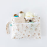 Bumkins Wet/Dry Clutch: Palm Daze holds travel bottles, a passport, and loofah on a white background.