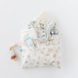 Baby essentials displayed in a Bumkins Wet/Dry Clutch: Palm Daze on a white background: clothes, pacifier, bottle, diaper.