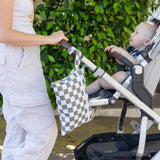 An adult pushes a stroller outdoors, carrying the Bumkins Wet Bag + Wet/Dry Clutch + Clear Travel Bag Set in Charcoal Check.