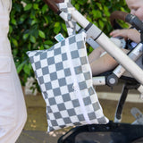 A bag from Bumkins Wet Bag + Wet/Dry Clutch Set: Charcoal Check hangs from the handle of a stroller with a child against greenery.