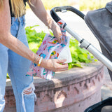Under sunny skies, someone in jeans tucks wipes into a colorful Bumkins Wet/Dry Clutch: Boots attached to a stroller amidst greenery.
