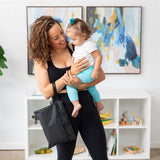 A woman in workout gear holds a smiling toddler and a Bumkins Wet/Dry Clutch: Rich Black in a bright room.