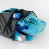 Bumkins Wet/Dry Clutch: Rich Black lays open on a white background, holding a blue bottle, shoes, towel, swimsuit, and sunglasses.