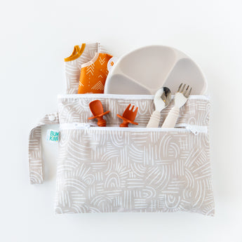 Bumkins Wet/Dry Clutch: Wander holds a divided plate, fork, spoon, bibs, and two orange utensils on a white background.