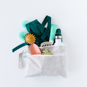 Bumkins Wet/Dry Clutch: Wander on white background with a swimsuit, turquoise shoes, sippy cup, sunscreen, and toys.