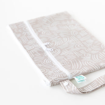 Bumkins Wet/Dry Clutch: Wander, a beige pouch with white patterns and waterproof fabric, sits flat on a white surface.