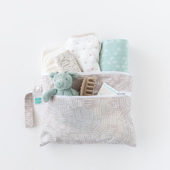 Bumkins Wet/Dry Clutch: Wander holds a stuffed dragon, clothes, hair clip, and wipes on a white background.