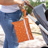 A person strolls through a park, pushing a stroller with a Bumkins Wet/Dry Clutch: Grounded hanging from the handle.