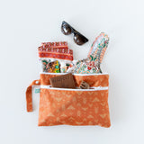 Bumkins Wet/Dry Clutch: Grounded lays on a white background, holding swimwear, passport, sunglasses, and a hair clip.