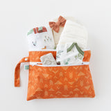 Bumkins Wet/Dry Clutch: Grounded holds a onesie, blanket, wipes, diapers, and a bow on a white background.