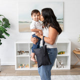 A woman kisses a child in a modern living room with a Bumkins Wet/Dry Clutch: Black on her arm.