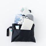 Bumkins Wet/Dry Clutch: Black holds baby essentials—wipes, lotion, diapers, cloth, sanitizer & pacifier—on a white background.
