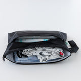 A compact Bumkins Wet/Dry Clutch: Black, slightly open to reveal clothes and diapers on a white background.