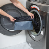 A person holds a Bumkins Wet/Dry Clutch: Black in front of a front-loading washing machine in a laundry room.
