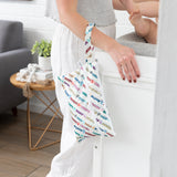 A person holds a Bumkins Wet/Dry Clutch: Mickey & Friends Varsity near a changing table in a bright room.
