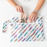 A child storing ballet shoes in a Bumkins Wet/Dry Clutch: Mickey & Friends Varsity on a white table.