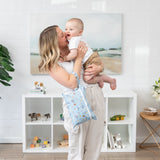 A joyful woman holds a laughing baby in a bright room, with a Bumkins Wet/Dry Clutch: Mickey + Minnie Sunny Side Up on her arm.